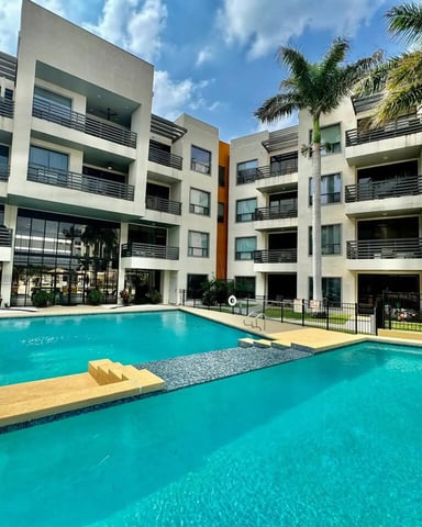 Modern apartment complex with two turquoise swimming pools, white buildings with balconies, and palm trees