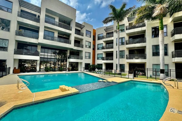 Modern apartment complex with two turquoise swimming pools, palm trees, and multi-story white buildings with balconies