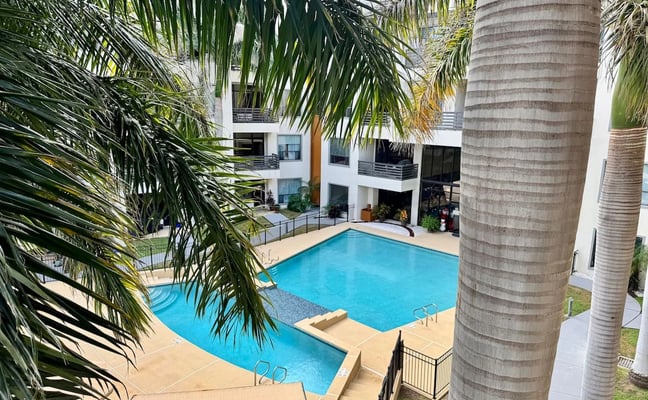 Courtyard with two swimming pools surrounded by white apartment building and palm trees