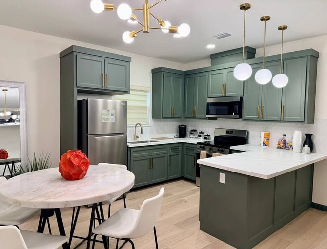 Modern kitchen with sage green cabinetry, white quartz countertops, stainless steel appliances, and brass pendant lighting over island.